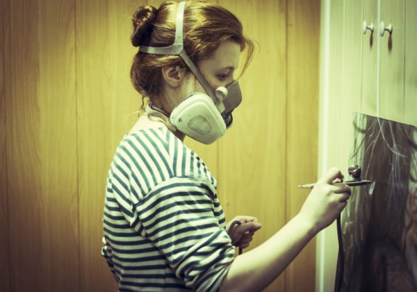 Artist in gas mask airbrushing painting in studio