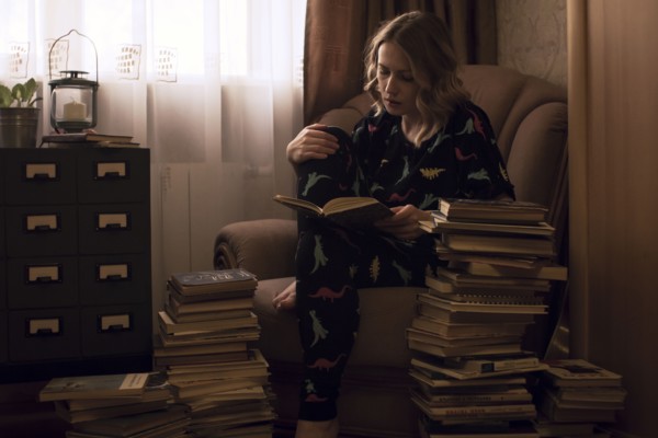 Caucasian woman sitting in armchair reading pile of books
