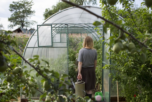 Caucasian woman carrying watering can to greenhouse