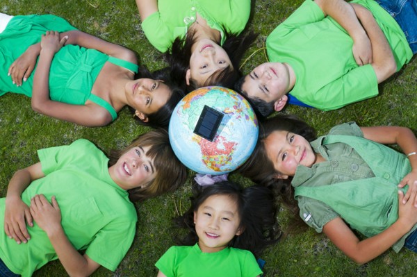 Children laying in grass around globe with solar panel