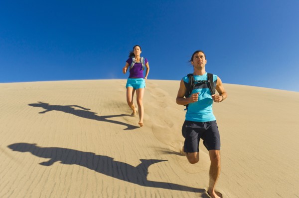 Hispanic couple running on sand dune