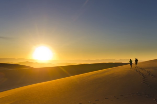 Hispanic couple walking on sand dune at sunset