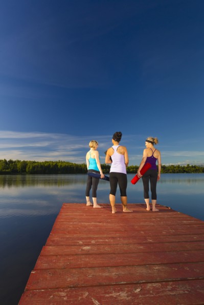 Women holding yoga mats on lake pier