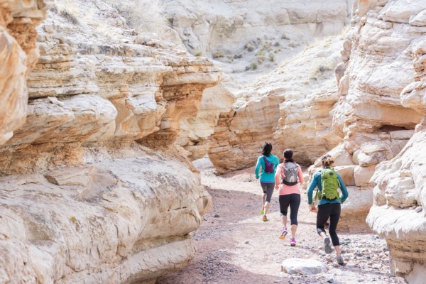 Women running in canyon wearing backpacks