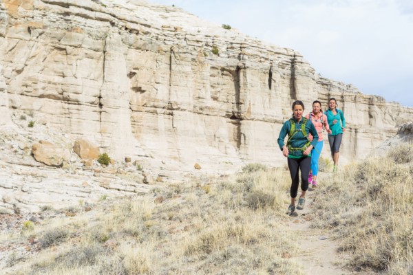 Women running in canyon wearing backpacks