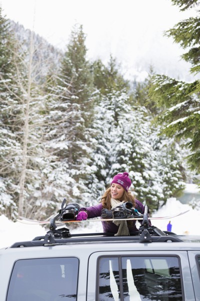 Caucasian woman checking snowboards in car roof rack