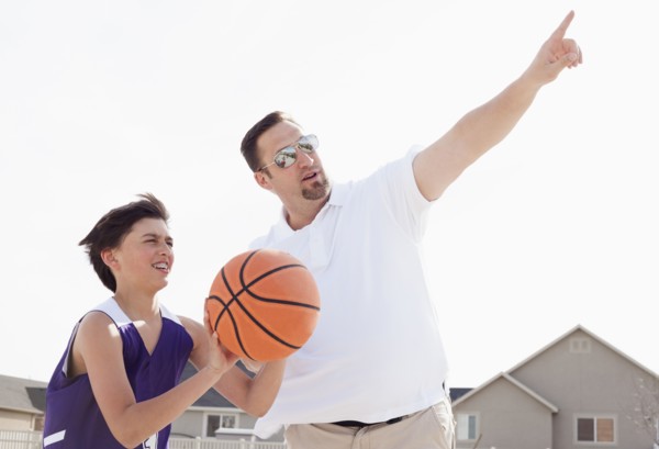 Father teaching son to play basketball in driveway