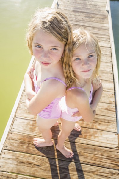 Caucasian girls standing back to back on dock