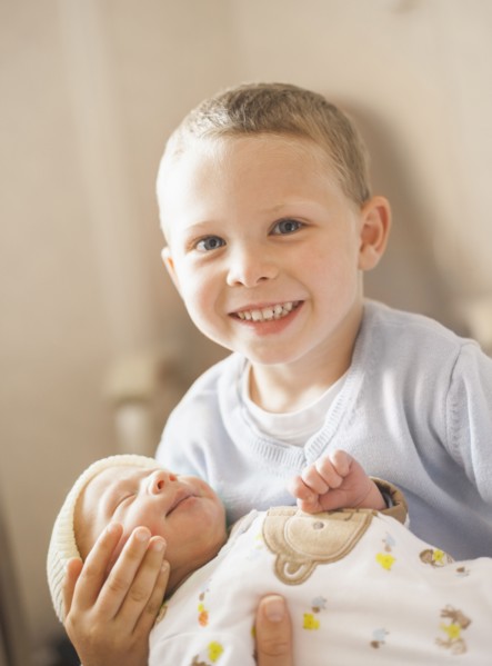 Caucasian boy holding newborn baby brother