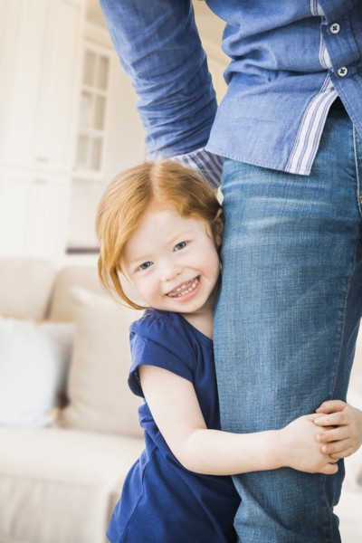 Caucasian girl clutching father's leg