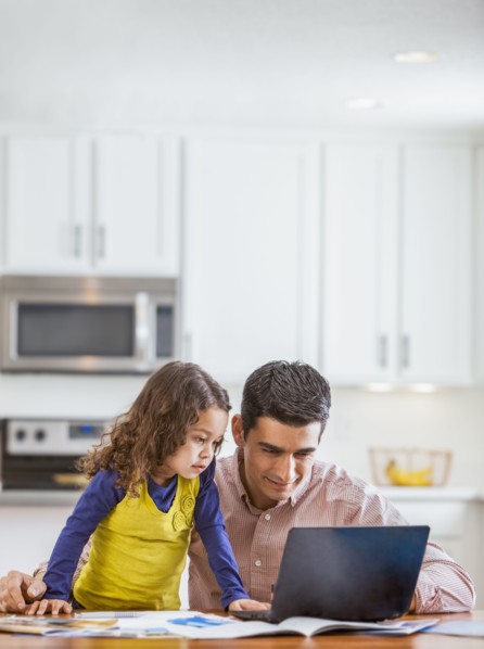 Father and daughter using laptop in kitchen