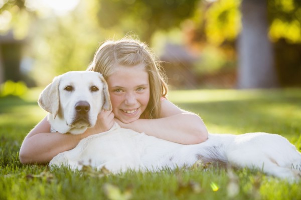 Caucasian girl hugging pet dog on grassy lawn