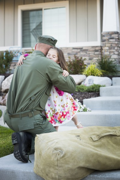 Returning Caucasian soldier hugging daughter on front stoop