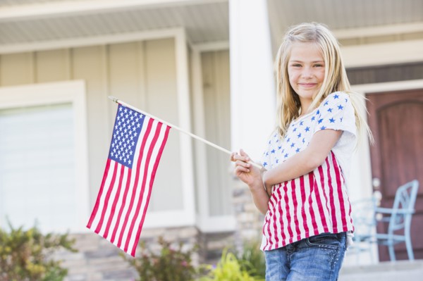 Smiling Caucasian girl waving American flag near house