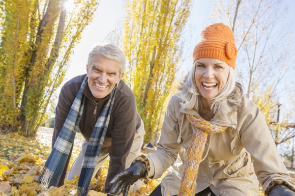 Older Caucasian couple playing in autumn leaves