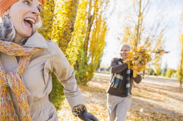 Older Caucasian couple playing with autumn leaves