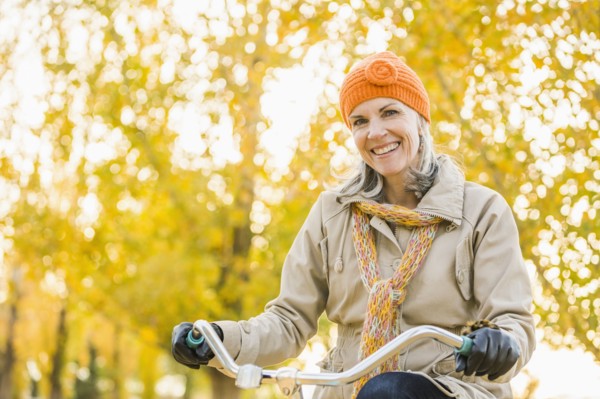 Older Caucasian woman riding bicycle under autumn trees