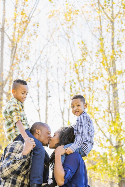 Parents carrying children on shoulders near autumn trees