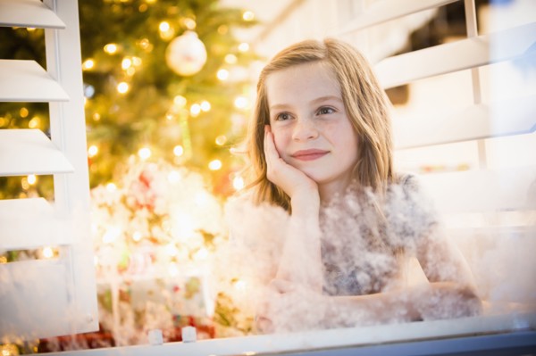Caucasian girl peering out window at Christmas