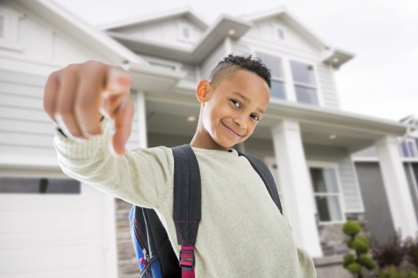 Black boy in backpack pointing on front lawn