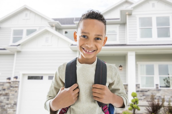 Black boy in backpack smiling outside house