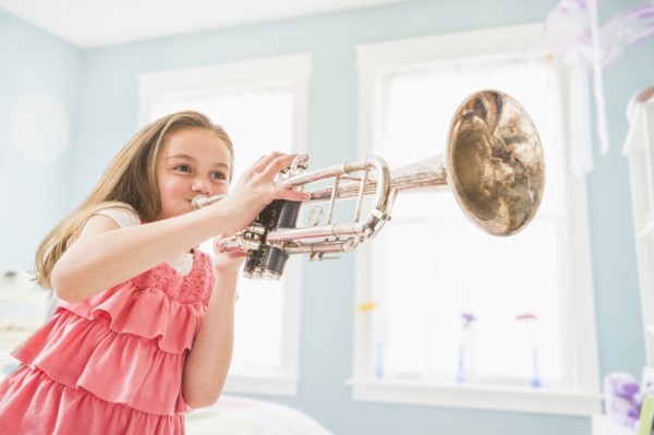 Caucasian girl playing trumpet in bedroom