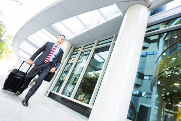 Mixed race businessman rolling luggage in office