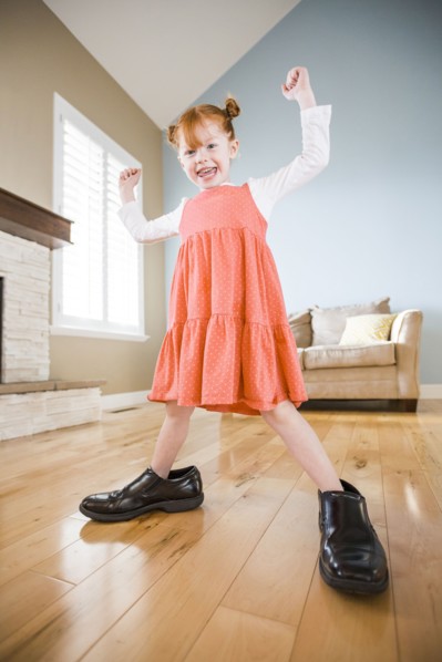 Caucasian girl wearing shoes of father in living room