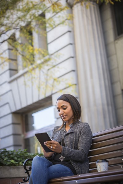 Indian woman sitting on city bench using digital tablet