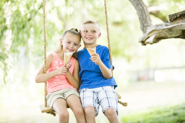 Caucasian brother and sister eating ice cream cones on rope swings