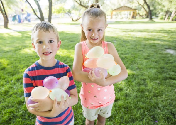 Caucasian brother and sister holding water balloons