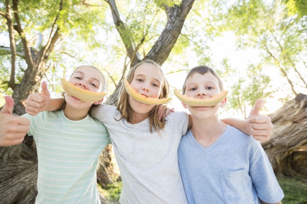 Caucasian boy and girls smiling with cantaloupe rinds
