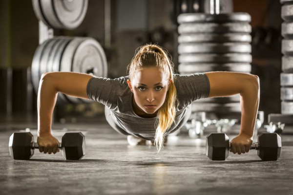 Caucasian woman doing push-up using dumbbells in gymnasium