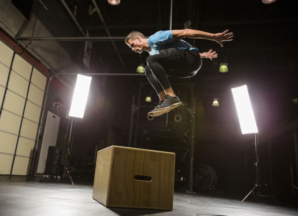 Caucasian man jumping on box in gymnasium