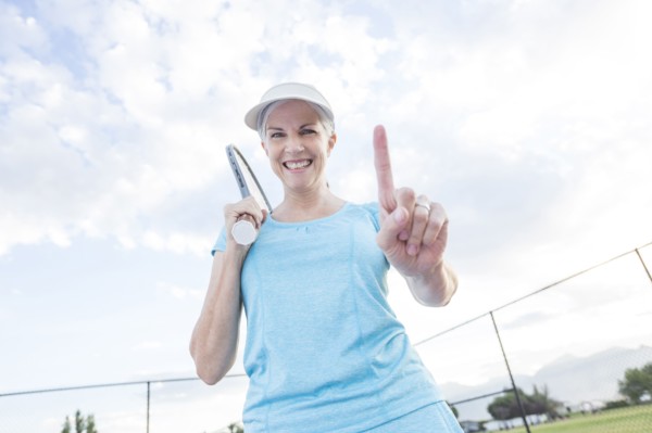 Caucasian woman holding tennis racket gesturing number one