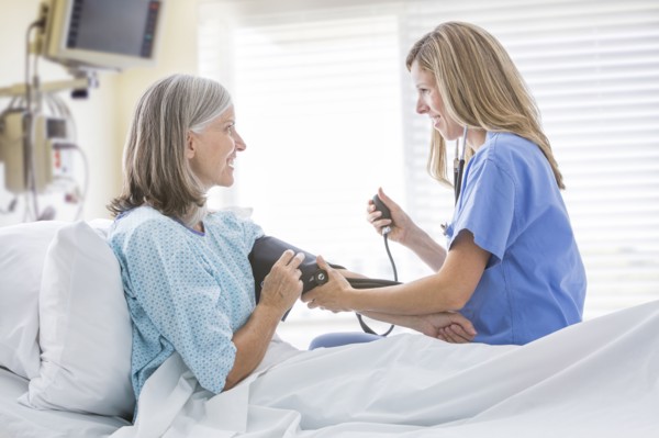 Caucasian nurse measuring blood pressure of woman in hospital bed