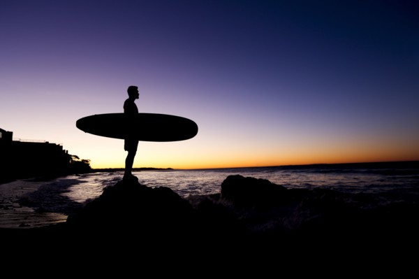Silhouette of Hispanic man holding surfboard at beach