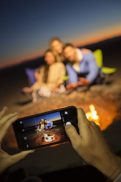 Hands of woman photographing friends on beach with cell phone