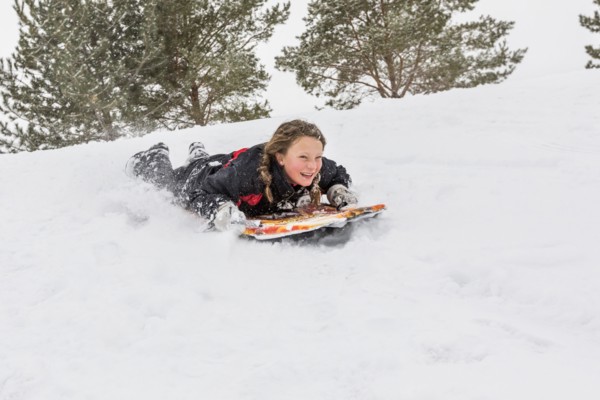 Smiling girl sliding on snowboard on hill in winter