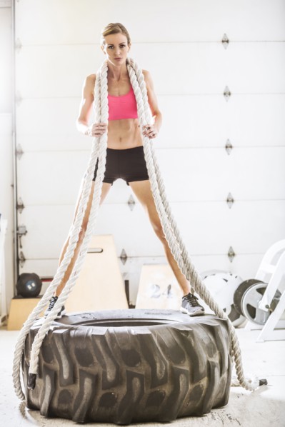 Woman holding heavy ropes standing on tire in gymnasium
