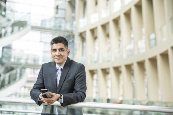 Mixed Race businessman leaning on railing in lobby holding cell phone