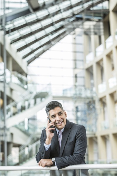 Mixed Race businessman leaning on railing in lobby talking on cell phone