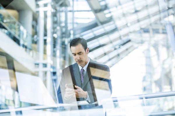Mixed Race businessman texting on cell phone leaning on railing in lobby