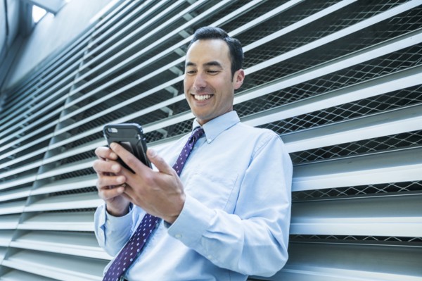 Smiling Mixed Race businessman leaning on wall texting on cell phone