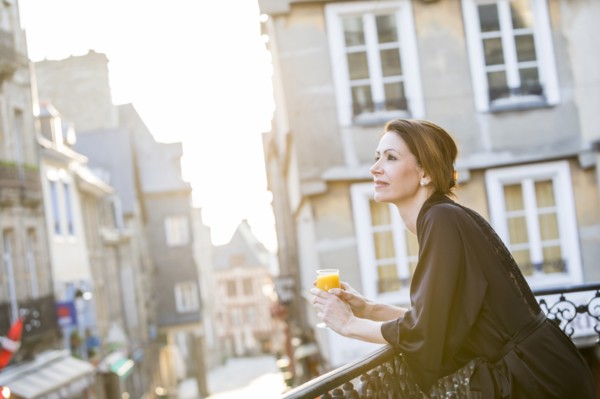 Caucasian woman drinking orange juice on balcony in city