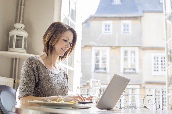 Caucasian woman typing on laptop and eating meal