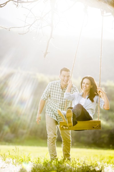 Man pushing woman swinging on tree swing