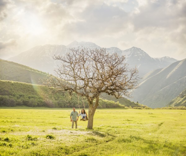 Man pushing woman swinging on tree swing