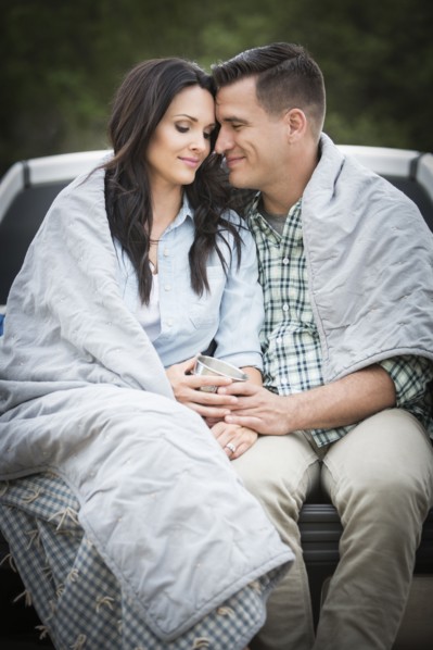 Couple wrapped in blanket sitting on bed of pick-up truck