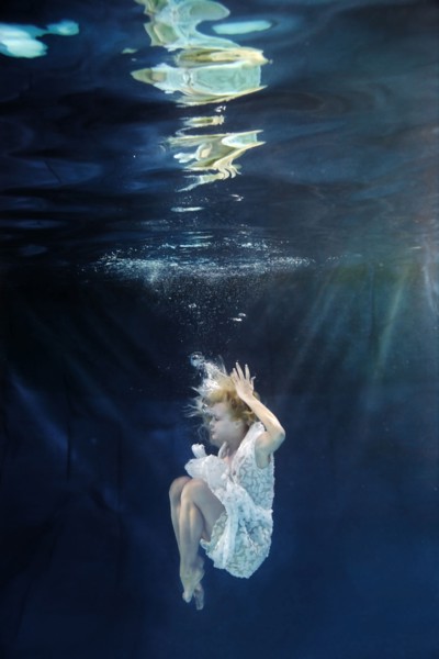 Caucasian woman in dress swimming under water